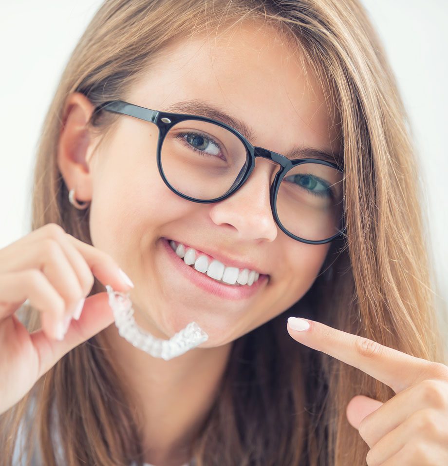 Young girl wearing black framed glasses and holding up an Invisalign Teen retainer