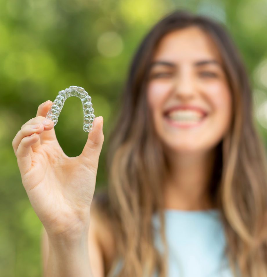 Young woman smiling holding out an Invisalign retainer